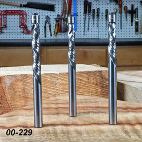 Three spiral upcut router bits for woodworking on a workshop bench with tools in background
