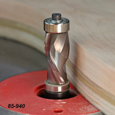 Spiral flush trim router bit shaping wood edge on a router table, close-up view.