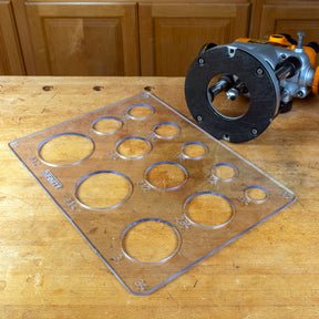 Acrylic circle and radius cutting template with various hole sizes on a woodworking bench next to a router tool.