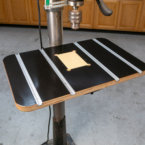 Drill press table with T-tracks and insert for woodworking, mounted in a workshop