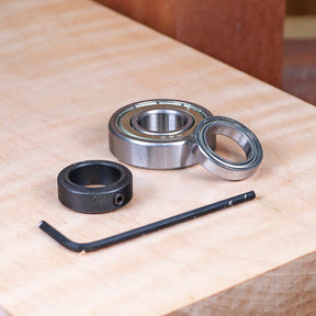 Router bearing kit with two ball bearings, black collar, and hex key on wood surface