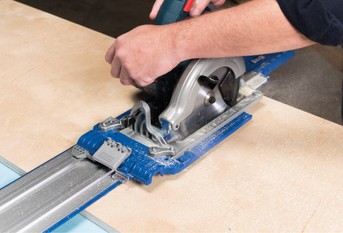 Person using a circular saw with a guide rail on a wooden surface