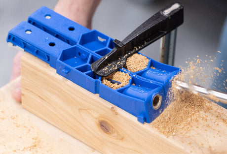 Pocket hole jig clamped to wood board with drill and wood shavings, woodworking tool in use