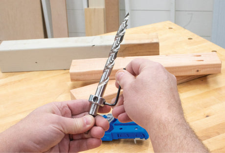 Person adjusting pocket hole jig drill bit with hex wrench on workbench for woodworking