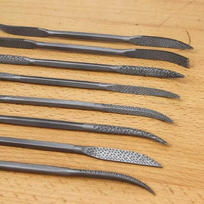 Set of eight curved woodworking rasps with textured blades on a wooden surface.