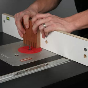 Hands using a router table with fence to cut finger joints in a wood board