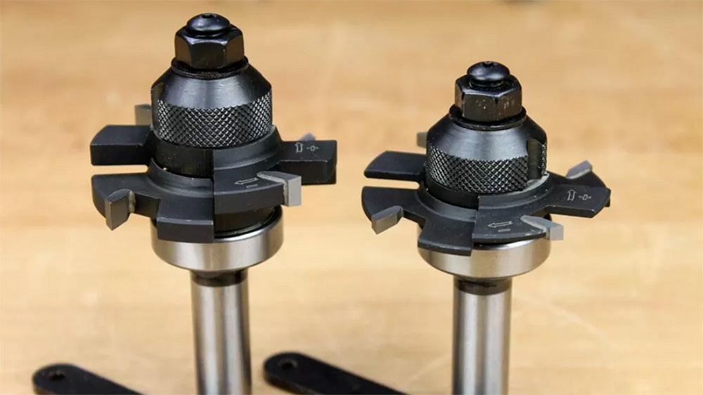 Two steel woodworking router bits with carbide-tipped cutting edges on a workshop table