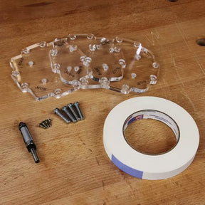 Router table template set with acrylic templates, screws, guide bushing, and tape on wood bench.