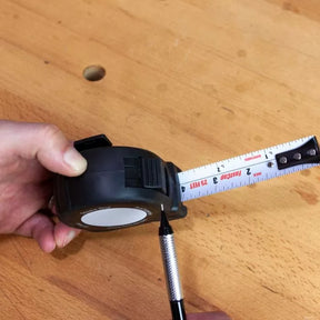 Hand holding a tape measure with a marking pencil on a woodworking table
