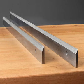 Pair of steel jointer knives on a wooden workbench, woodworking tool accessories