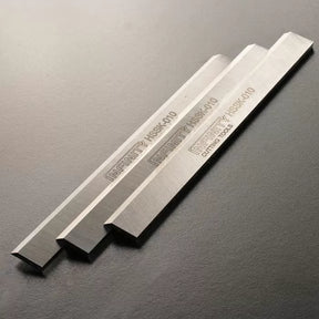 Set of three high-speed steel planer blades for woodworking tools on a dark background.