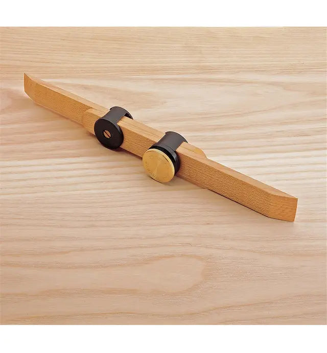 Woodworking marking gauge tool with brass and black accents on a light wood surface