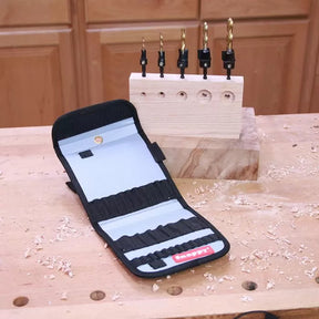 Woodworking drill bit set with case on workbench, block showing drilled holes