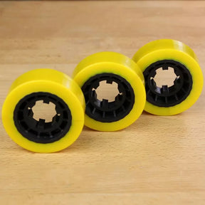 Three yellow woodworking feeder wheels with black centers on a wooden surface
