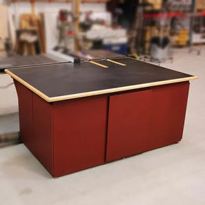 Large woodworking outfeed table with black work surface and red base in workshop setting