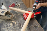 Person using a drill to assemble wooden dowels on a workbench with nails and glue nearby.