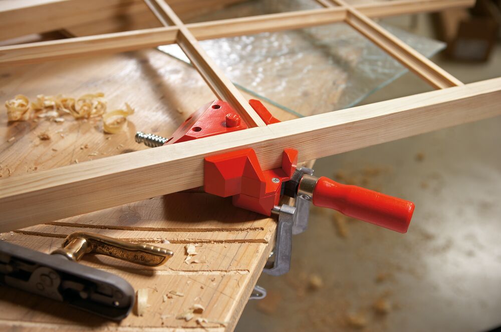 Woodworking scene with a red clamp holding wooden planks together on a workbench.
