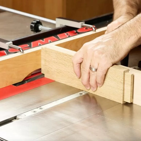 Woodworker using a table saw with a miter gauge to cut a dado joint in a wooden board.